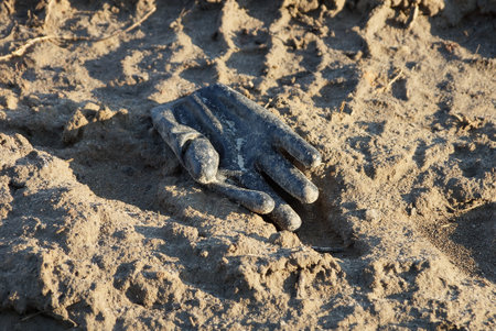 garbage from one old black dirty rubber glove lies on brown ground outsideの写真素材