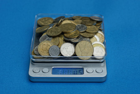 small gray electronic scale full of yellow coins stands on a blue table