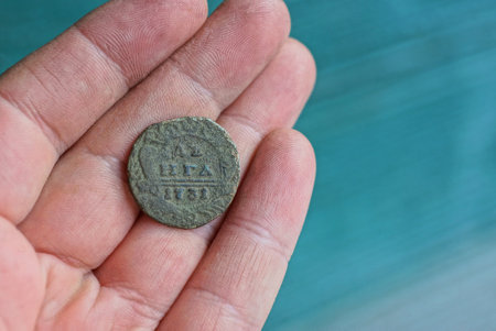 one old copper coin lies on the fingers on a hand on a green background