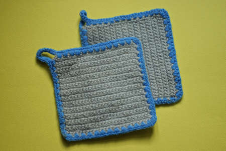 two gray knitted square napkins made of woolen fabric lie on a yellow tableの写真素材