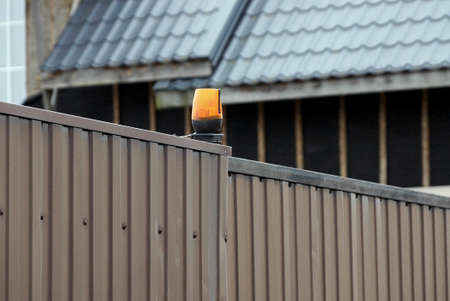 one red signal lamp on the brown metal wall of the fence at the closed gate