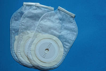 three white medical plastic colostomy bags on a blue backgroundの写真素材