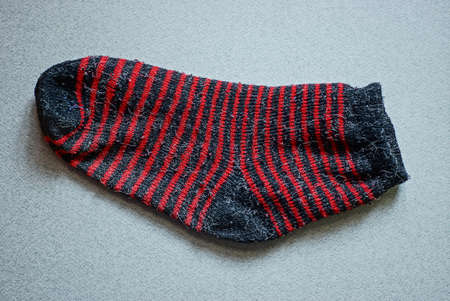 one old woolen striped red black sock lying on a gray tableの写真素材