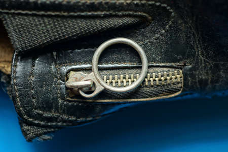 closed gray metal zip with a ring on black leather clothes lies on a blue tableの写真素材