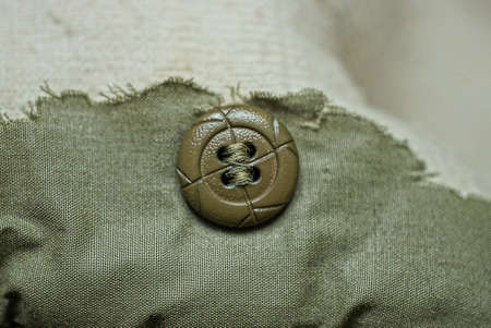 one large plastic button on a torn piece of green fabric on clothesの写真素材