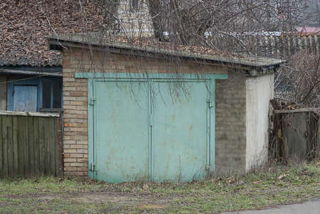 one old brown brick garage with a metal gate and a fence in the streetの写真素材