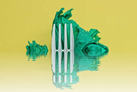 part of a white plastic fork with a piece of green paper in water on a yellow background
