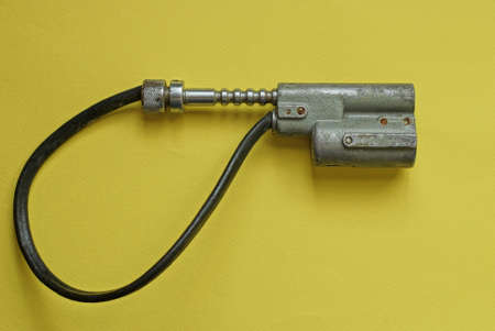 one old closed bicycle lock with a gray metal core and a black cable lies on a yellow tableの写真素材
