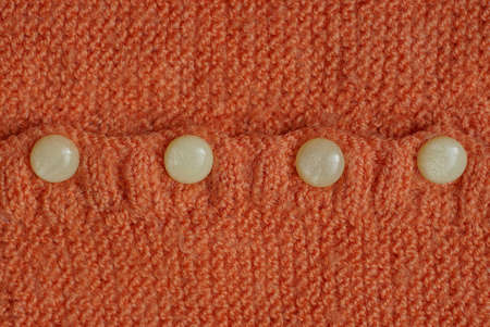 four small gray plastic buttons on the orange woolen fabric of the garment