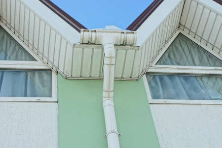 white plastic gutter pipe in the snow on a green gray wall with windows on the street
