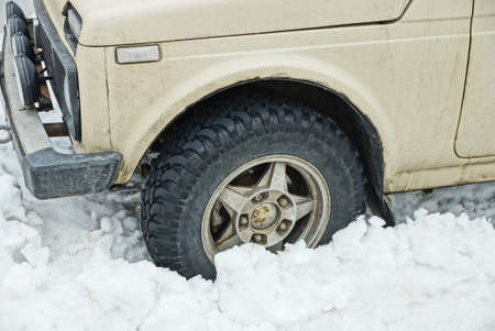 one black wheel of a gray car in a white snowdrift on a winter street