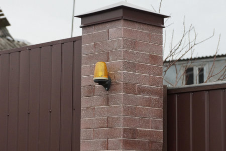 yellow signal light hanging on a brown brick wall of a fence on the street