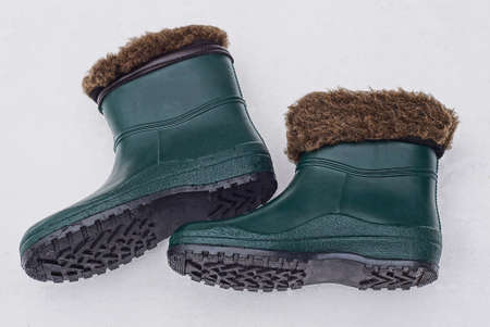 two green rubber boots with brown fur lining lies on white snow on a winter street