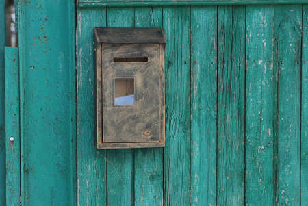 one brown gray metal mailbox hanging on a green wooden fence in the street