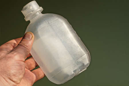 hand holds one plastic medical bottle on green background