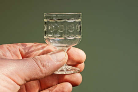 fingers on hand are holding one small empty crystal glass on gray background