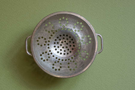 one old gray metal bowl a colander stands on a green tableの写真素材