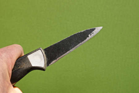 hand holds a black old knife on a green background