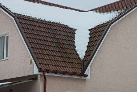 part of a brown tiled roof of a private house under white snow on a winter street