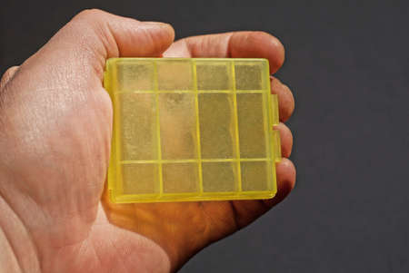 hand holds small yellow plastic box on gray background