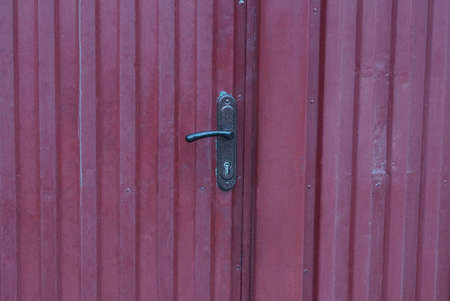 one black metal doorknob on a red closed iron door on the streetの写真素材