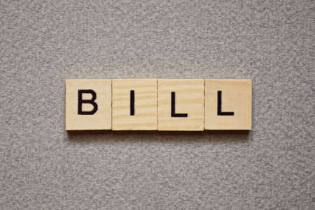text the word bill from brown wooden small letters with black font on an gray table