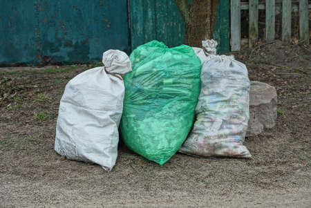 three large plastic garbage bags stand on the ground in dry grass outsideの写真素材