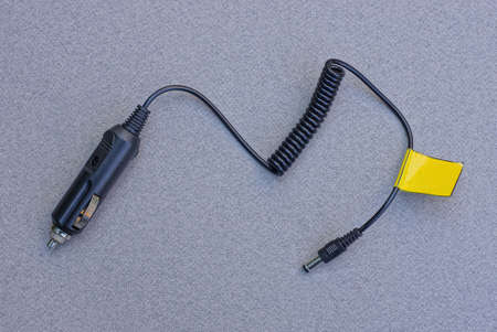 a black car charger with an electric wire and a plug lies on a gray table