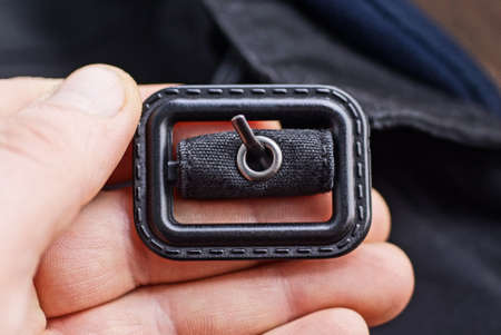 fingers hold a one closed black metal carabiner on a harness made of fabric