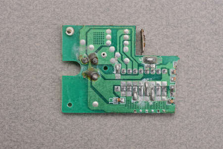 one green old plastic microcircuit with lead soldering lies on a gray table