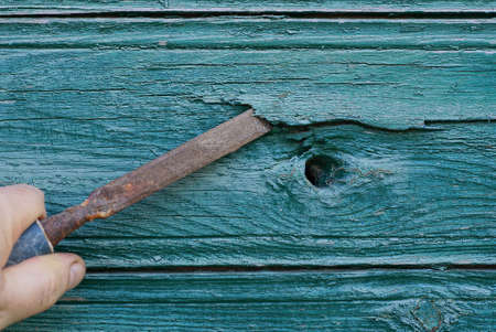 hand holds brown old rusty iron chisel in green wood plank wall