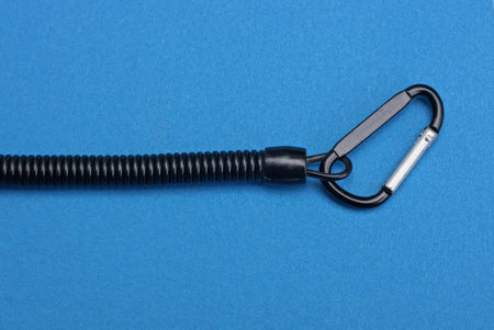 one metal carabiner latch on a black spiral wire lies on a blue table