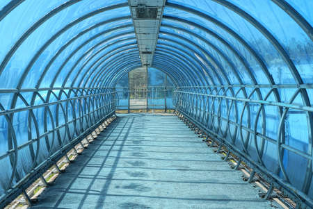 long pedestrian walkway inside with blue plastic cover and iron handrails on the concrete floorの写真素材