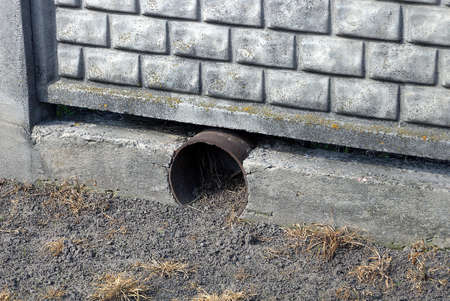 black metal gutter pipe in gray concrete fence wall on the ground outside