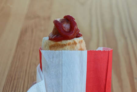 hot dog sausage in dough in red sauce and paper packaging lies on a white napkin on a brown backgroundの写真素材