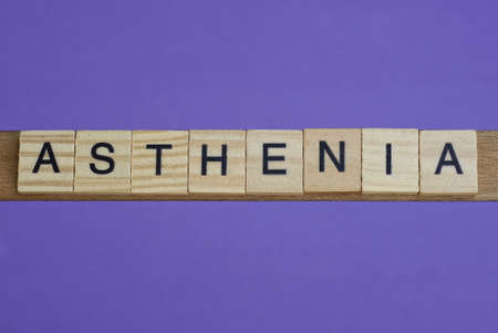 word asthenia in small square wooden letters with black font on a lilac backgroundの写真素材