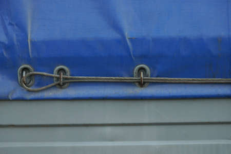 a piece of blue tarpaulin on a metal gray side of a car trailer with an iron cable in the loopsの写真素材