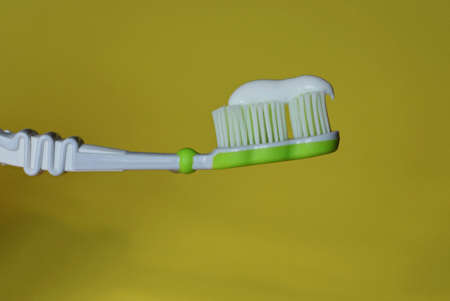 one plastic toothbrush with white toothpaste on yellow background