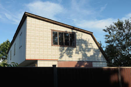 white brick attic of a private house on window behind a brown fence against a blue sky