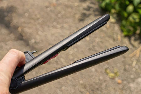 hand holds an long electric hairdryer with a black metal hair curler on a gray background