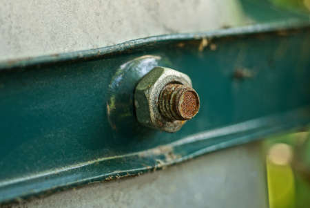 one rusty screw with a twisted nut on a green metal plate on an iron gray wallの写真素材