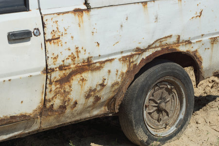 part of an old white passenger car in brown rust with a black wheel on gray sand in the streetの写真素材