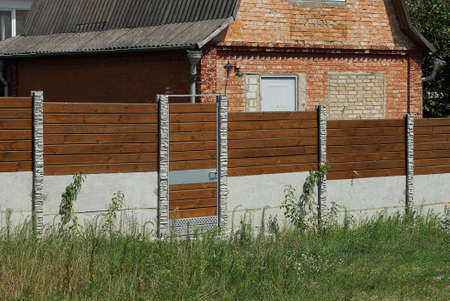 brown closed door and part of wooden fence wall on gray concrete foundation outdoors in green grassの写真素材