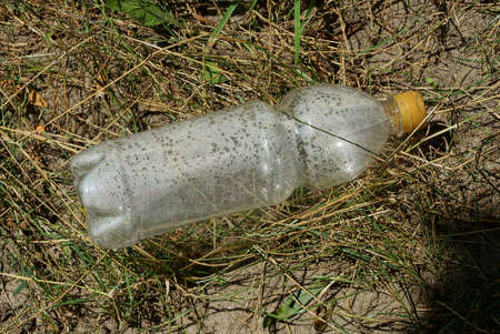 garbage from one big white plastic bottle lies on gray dry grass and ground in natureの写真素材