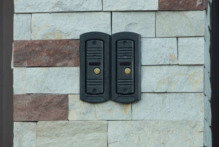 two black metal electric bells on gray brown bricks fence wall on the streetの写真素材