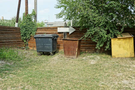 three garbage cans stand in green grass outside by a brown wooden fence wallの写真素材