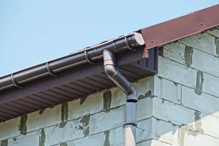 brown plastic gutter pipe on white brick wall outdoors against blue sky