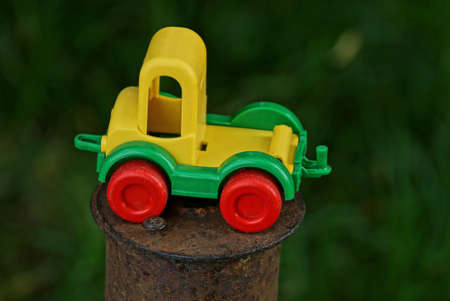 one small plastic colored toy car stands on a brown rusty iron pole outside on a green backgroundの写真素材