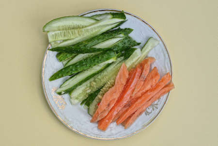 food from sliced green fresh cucumbers and pieces of sea red fish on a white plate on a yellow table