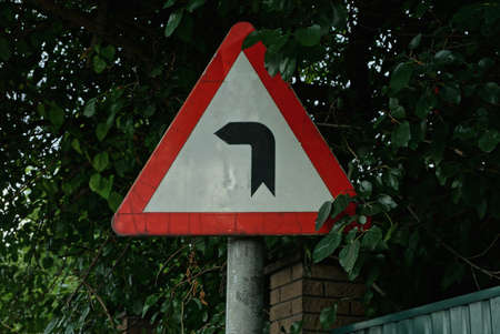 one triangular road sign dangerous turn of the road on a pole on the street in green vegetationの写真素材